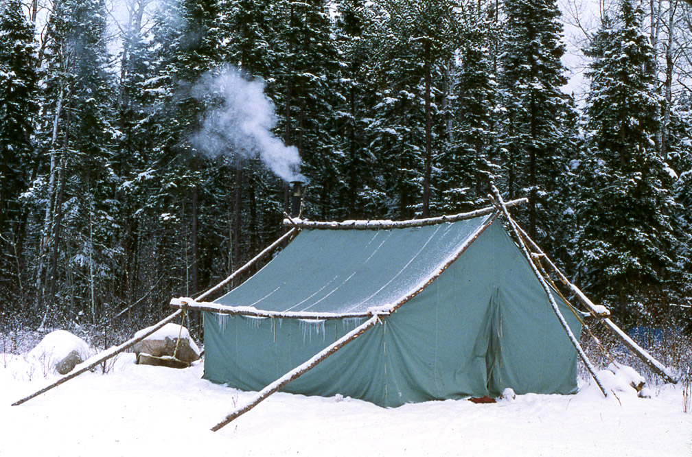 Doc's wall tent in the snow, with white snow coming out of the wood stove's chimney.